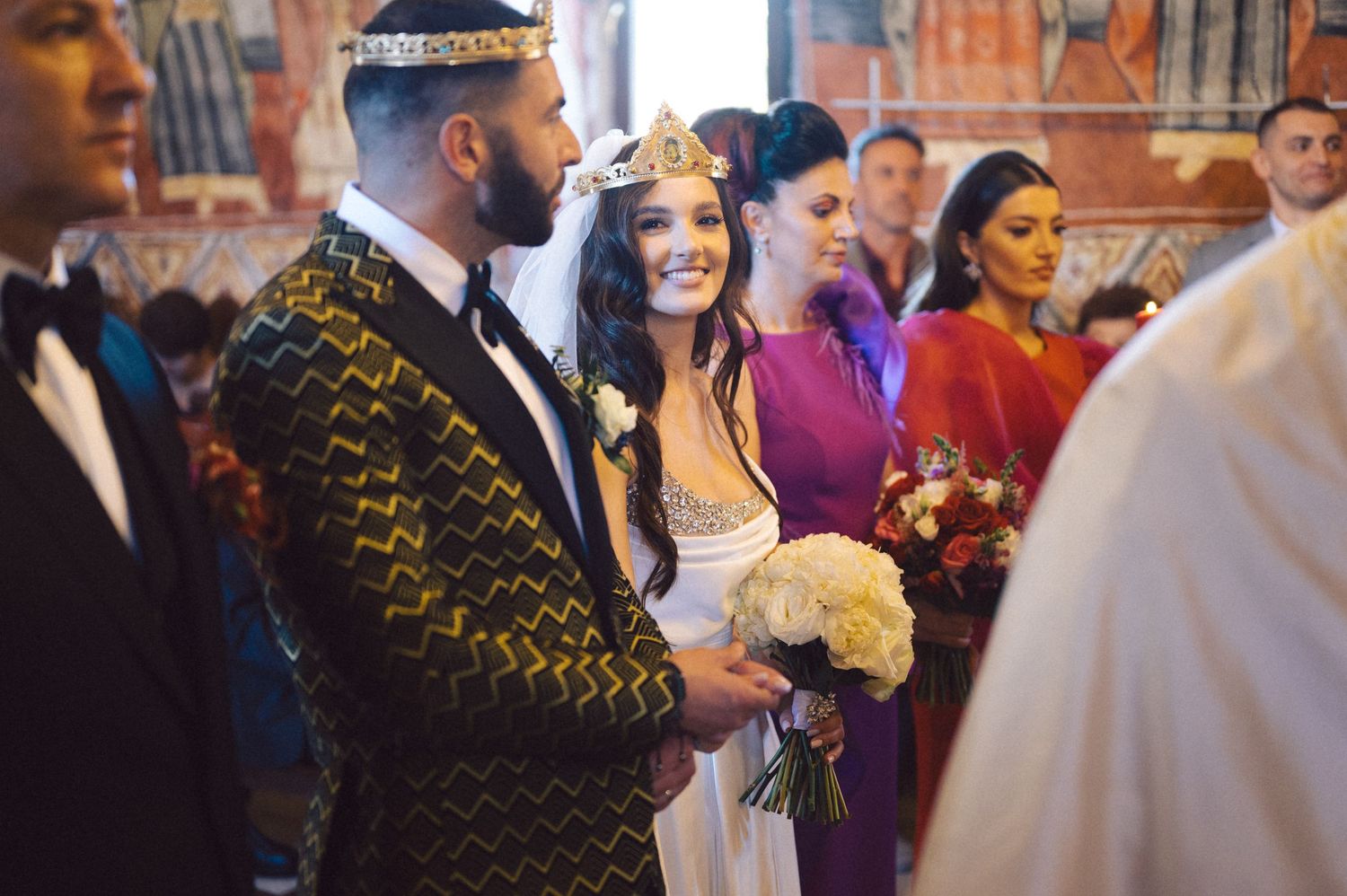 Wedding ceremony in an ornate church featuring guests in vibrant formal attire.