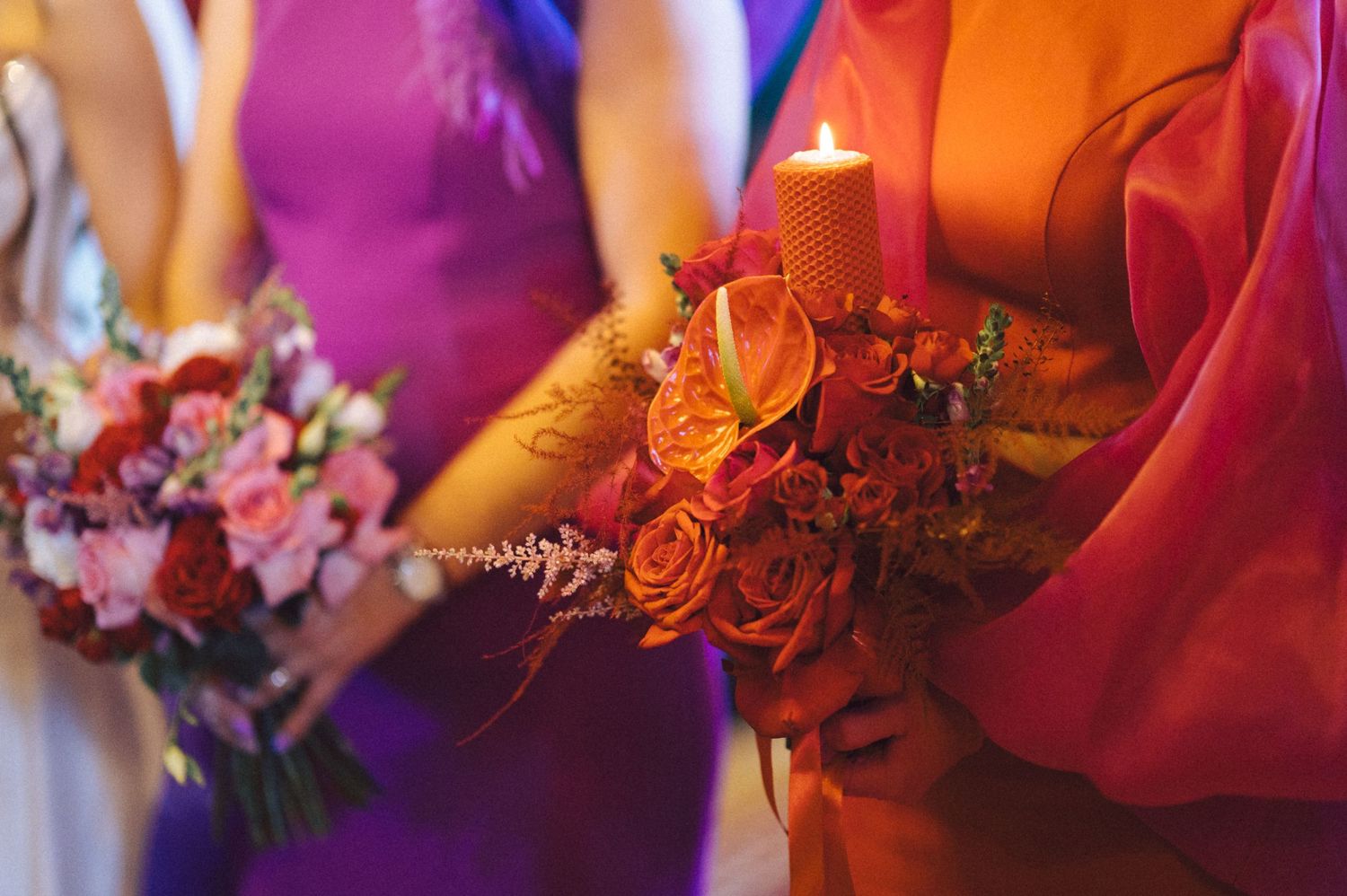 Close-up of colorful wedding bouquets with roses held by bridesmaids in purple and orange dresses.