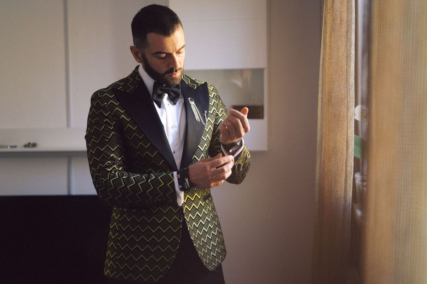 An elegant gold and black geometric patterned tuxedo being adjusted indoors.