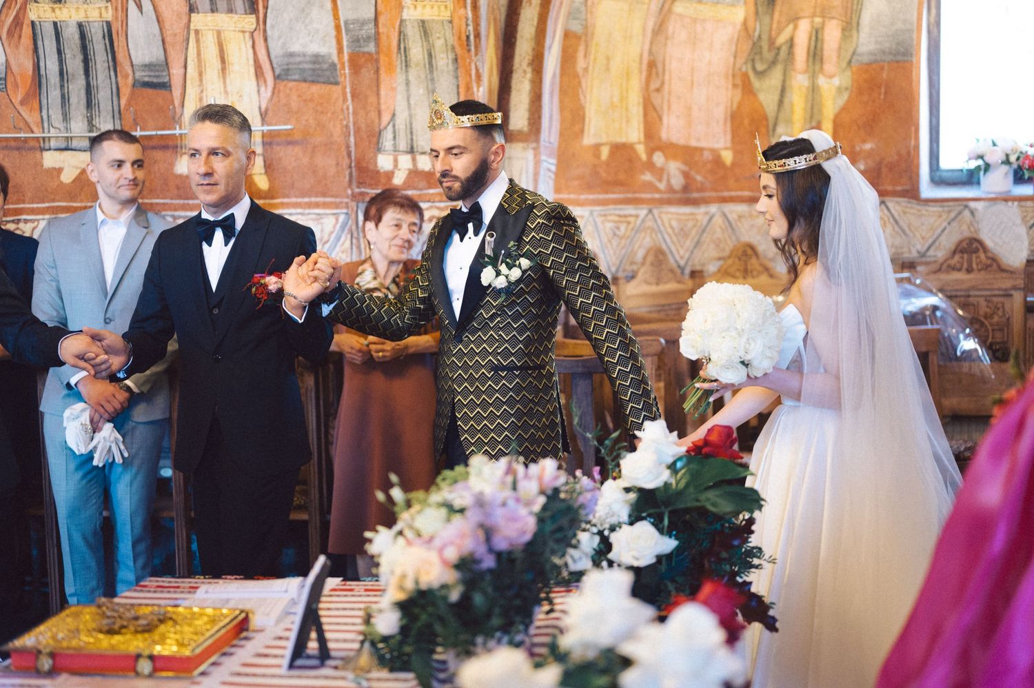 Orthodox wedding ceremony with guests and floral decorations in a historic church setting.