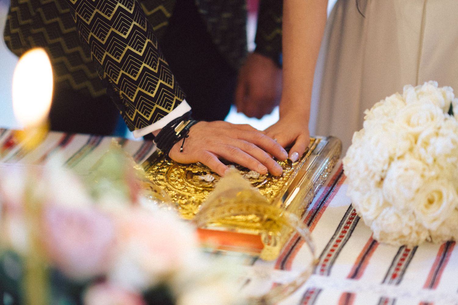 Close-up of hands on a decorative table with traditional embroidered linens and white floral arrangements.