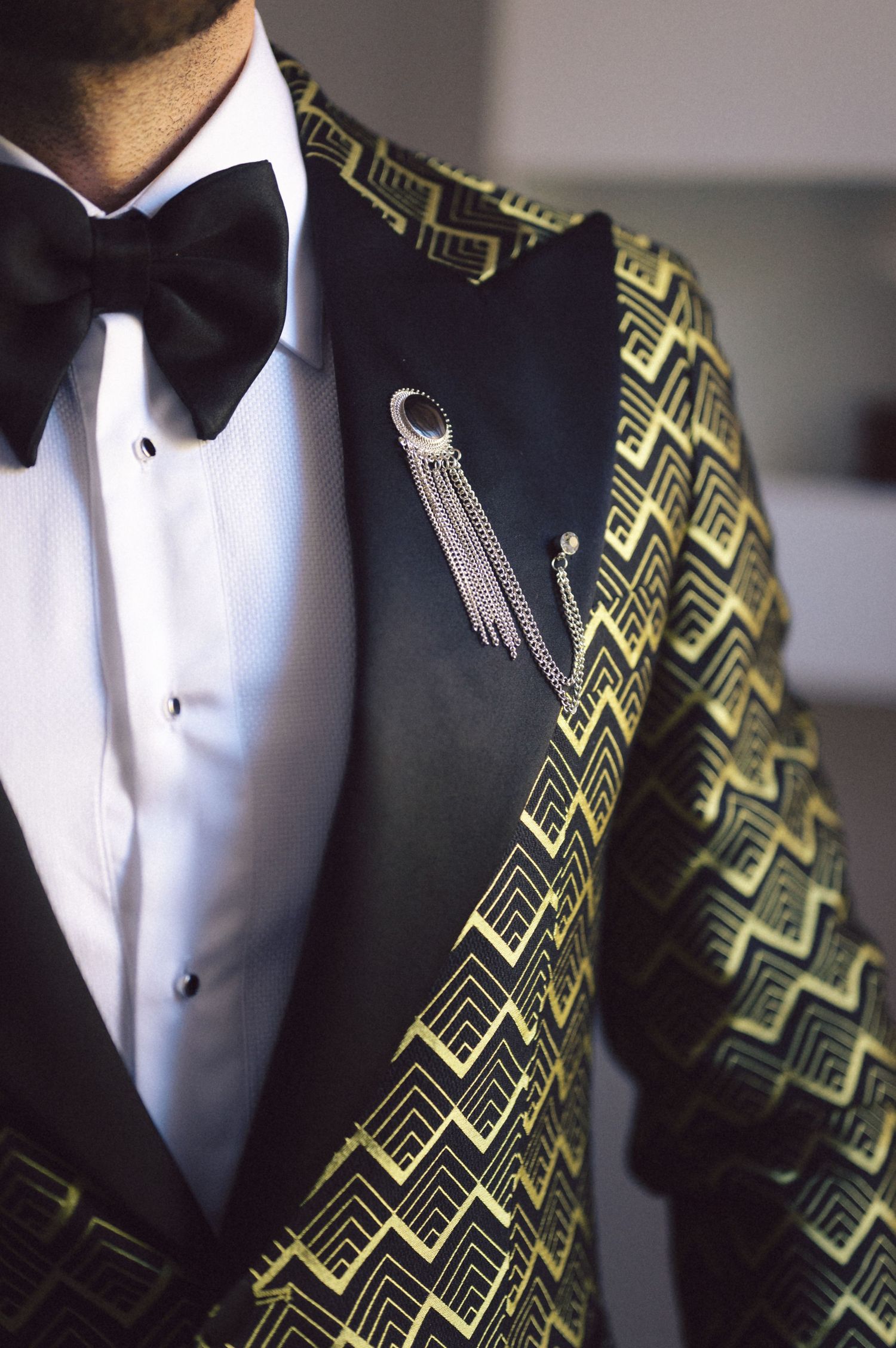 Detail shot of a black and gold geometric patterned tuxedo with bow tie and silver brooch.