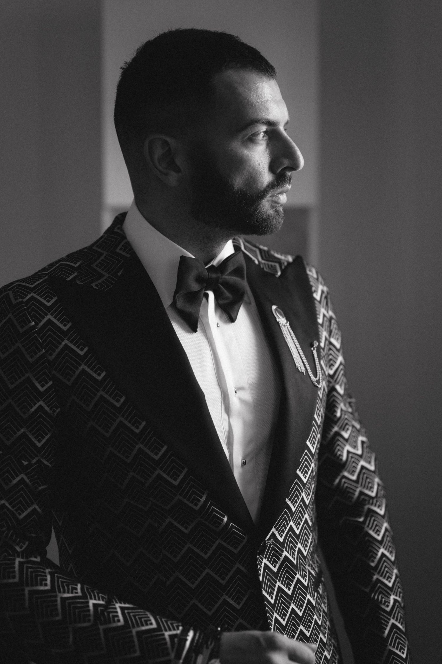 Side profile of a formal black and gold patterned tuxedo in dramatic lighting.