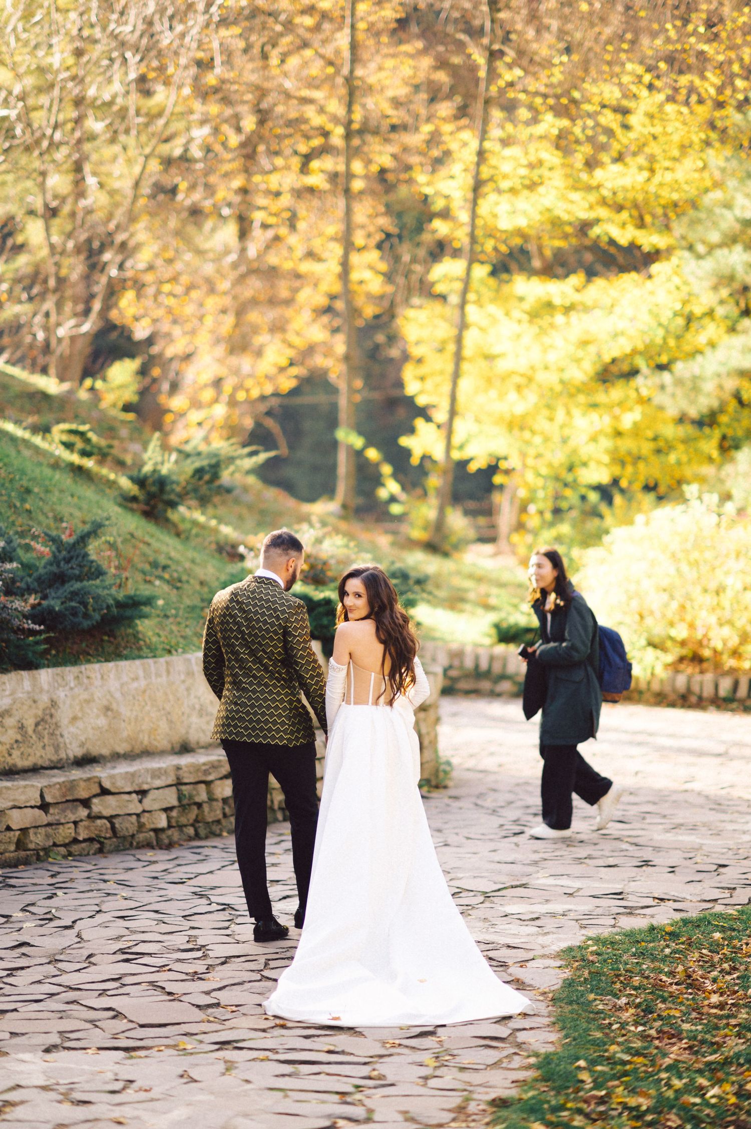 Couple walking on stone path surrounded by vibrant fall foliage in a romantic garden setting.