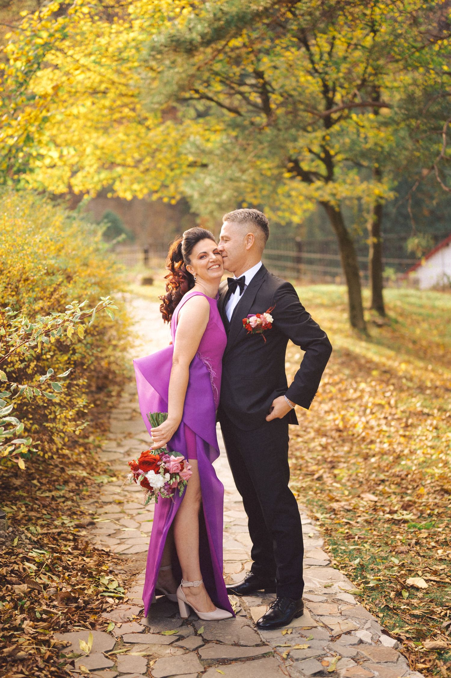 Elegant couple embracing on stone path surrounded by golden fall foliage.