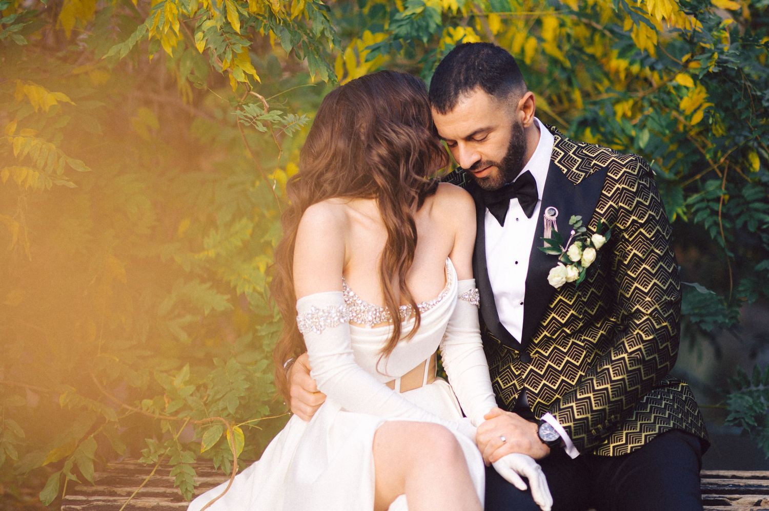 Romantic wedding couple embracing outdoors with gold patterned tuxedo jacket.