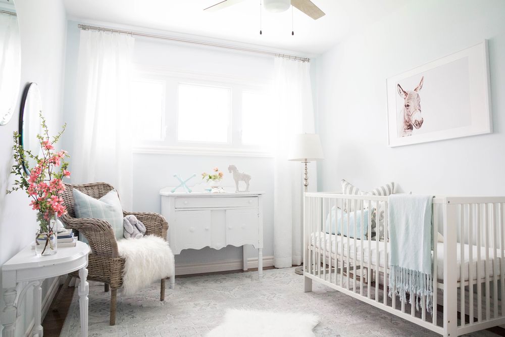 Serene white nursery with crib, rocking chair, floral arrangement and soft natural lighting.