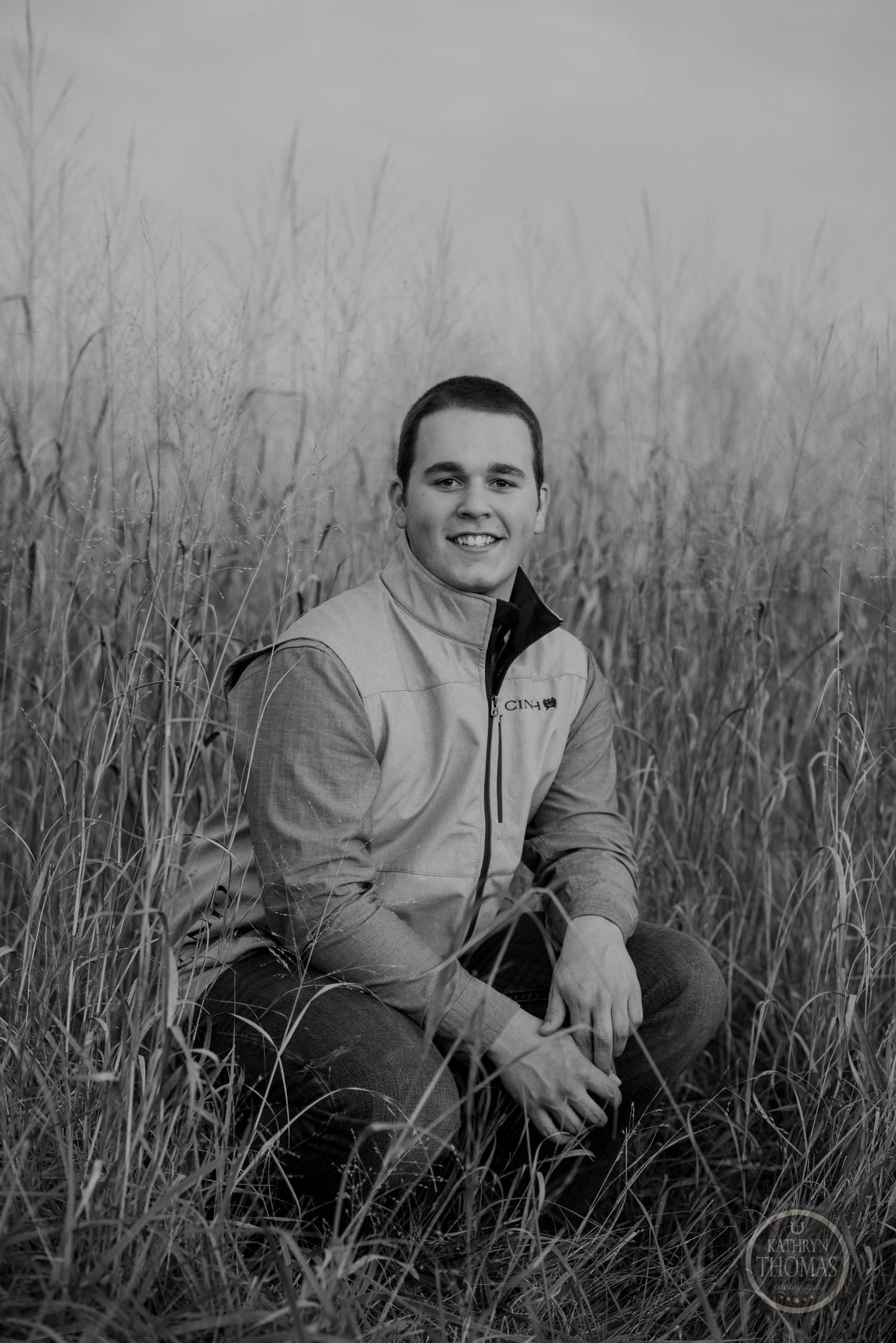 Outdoor portrait of person in gray fleece vest sitting in tall grass at dusk.