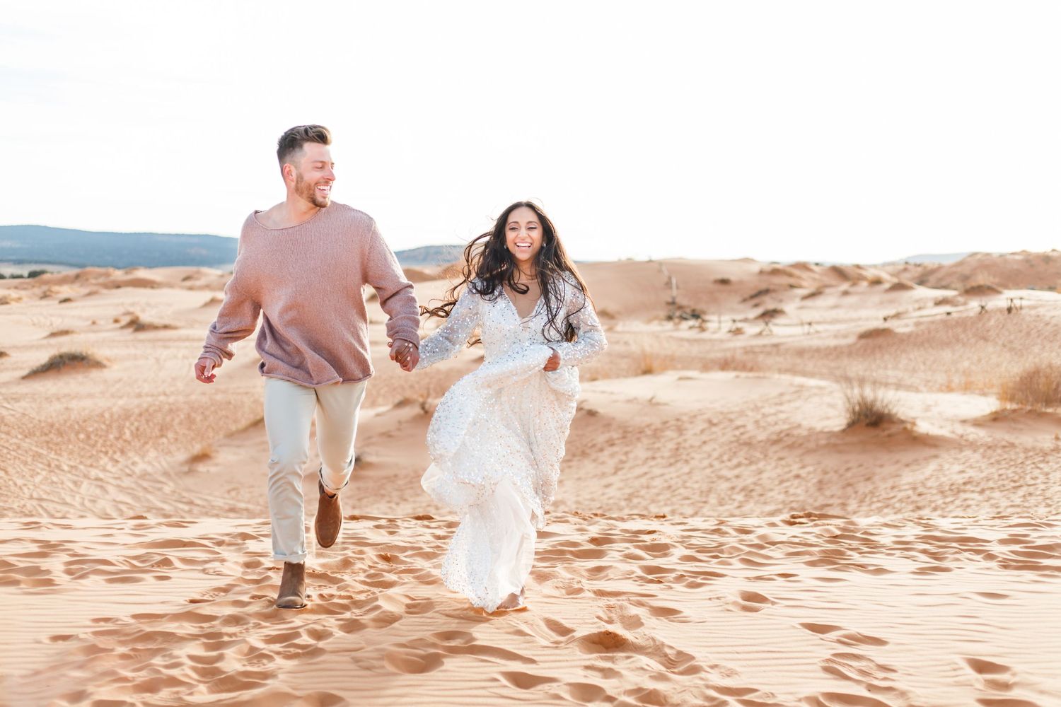 Couple runs hand in hand through desert sand dunes in romantic photoshoot at Coral Pink Sand Dunes, UT.