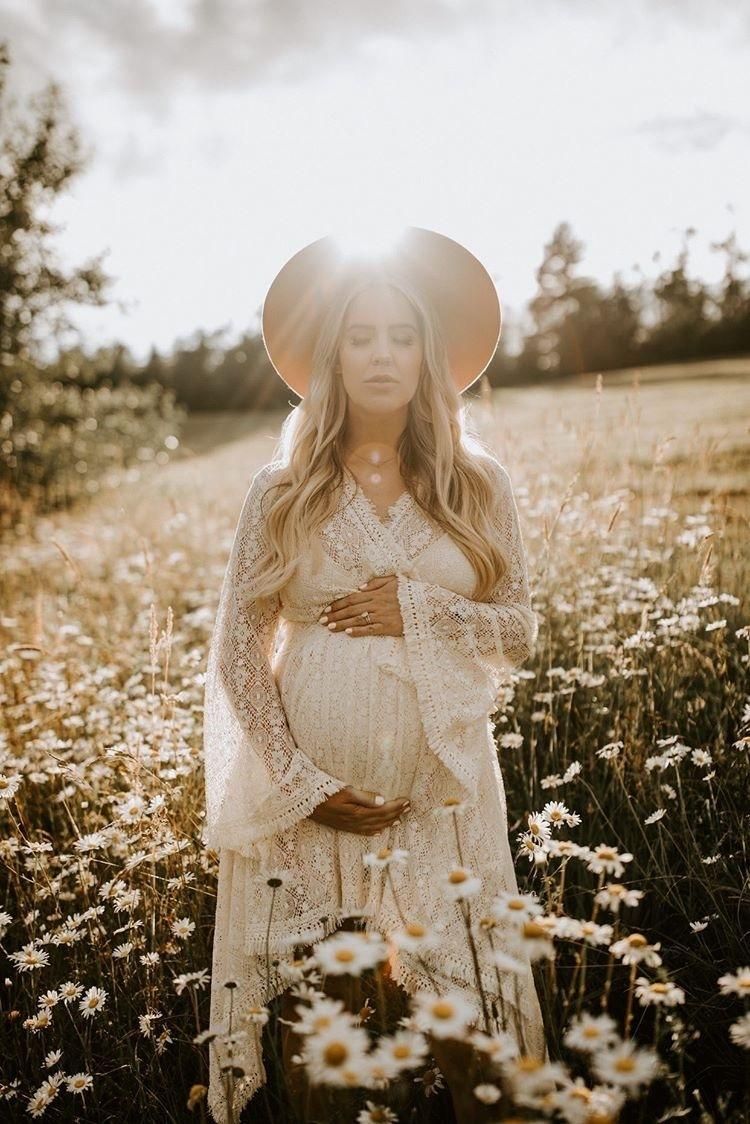 Ethereal maternity photo of woman in white dress standing among wildflowers at golden hour.