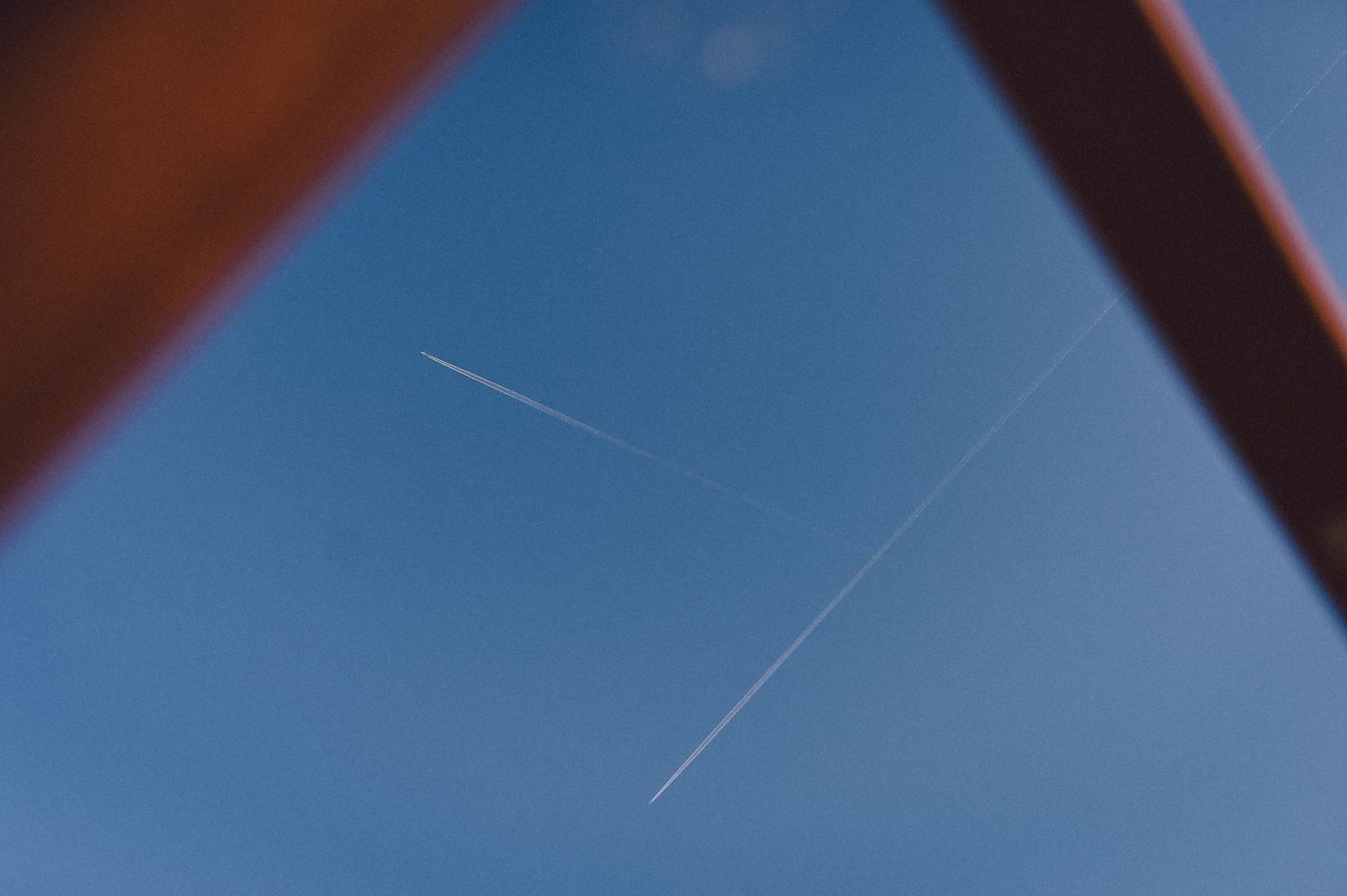 Airplane contrails crossing in a bright blue sky viewed through an angular frame.