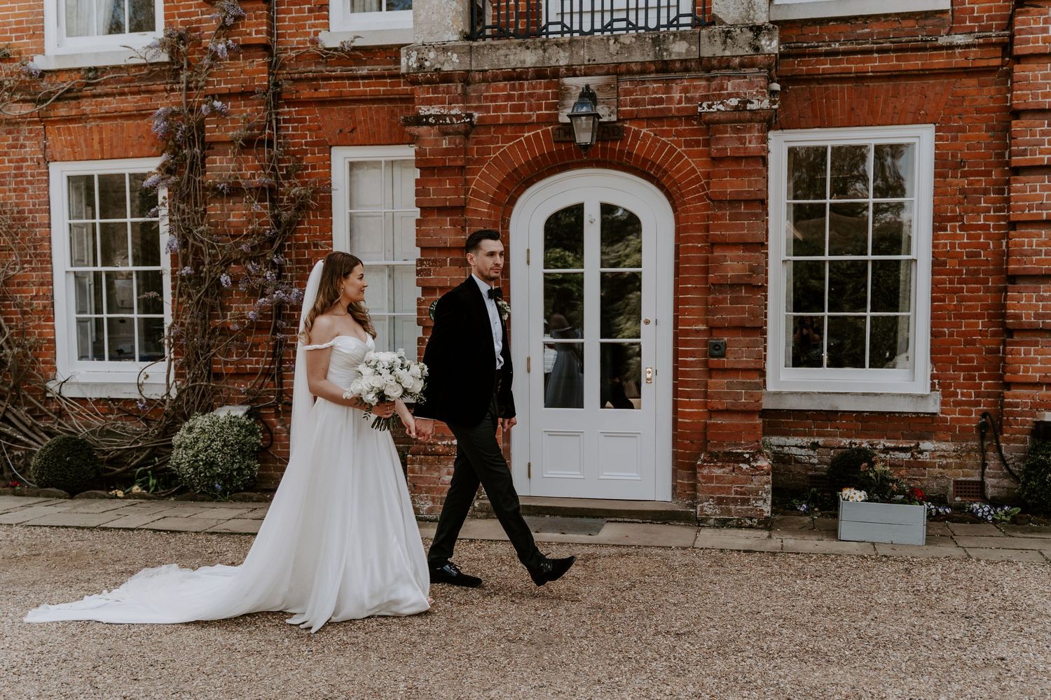 a bride and groom walking in front of a red brick hotel with sash windows.