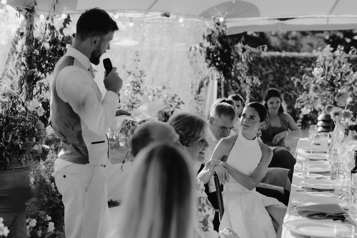 bride sat watching groom give his speech at marquee wedding in islip in oxfordshire