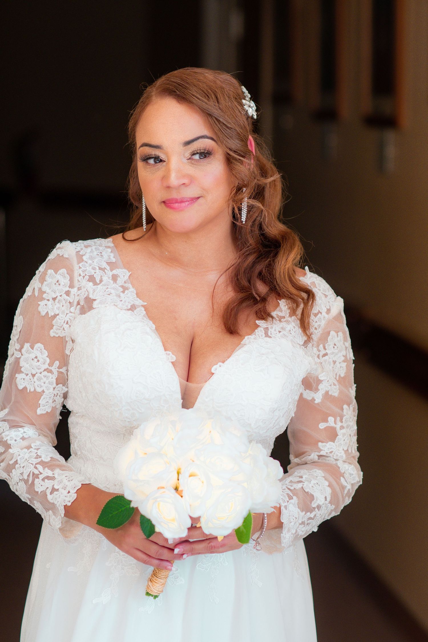 Close-up of a bride in a white lace long-sleeve wedding dress holding a white bouquet.