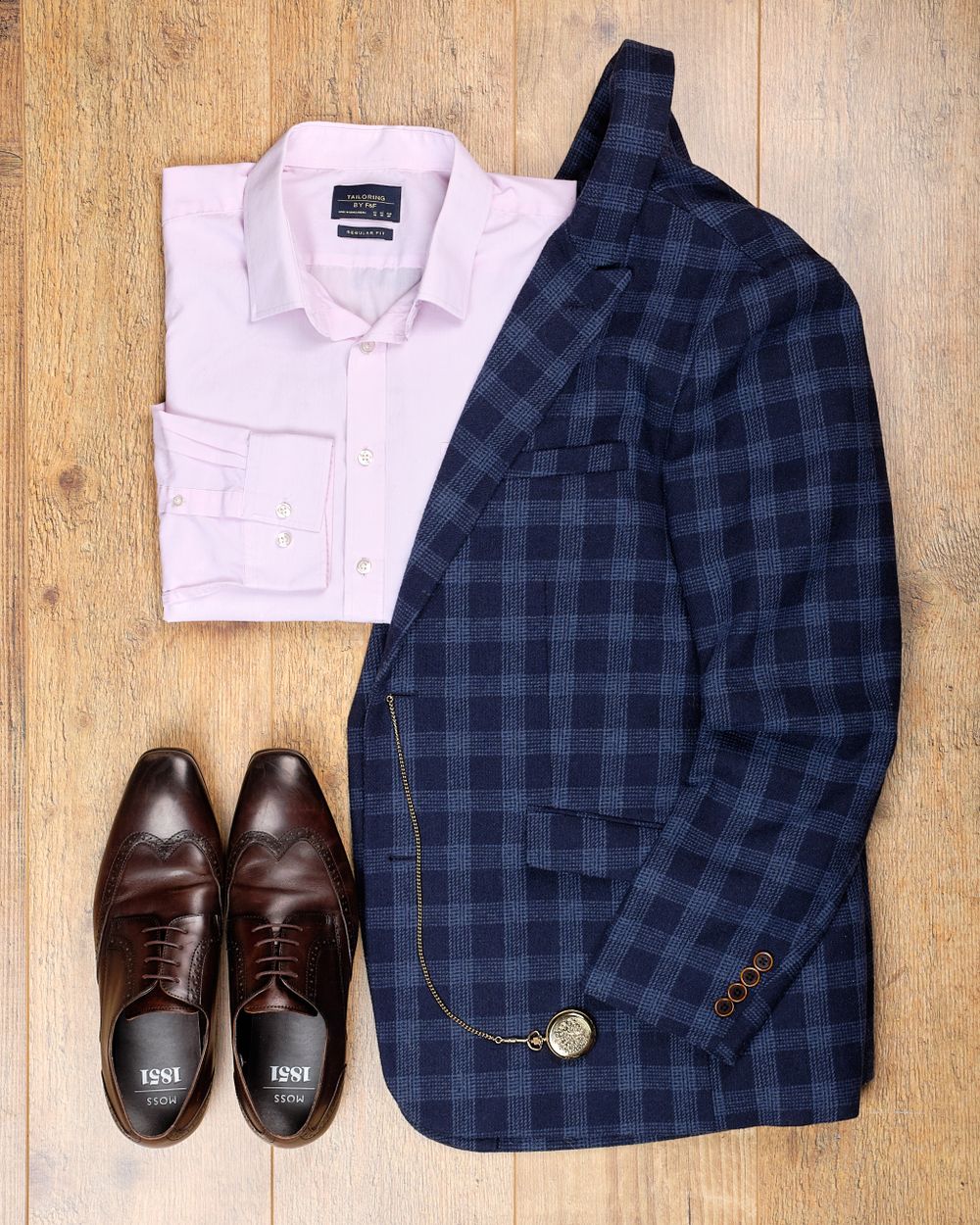 Flatlay of Cotton Traders jacket, F&F pink shirt and Moss Bros shoes on a light oak background.