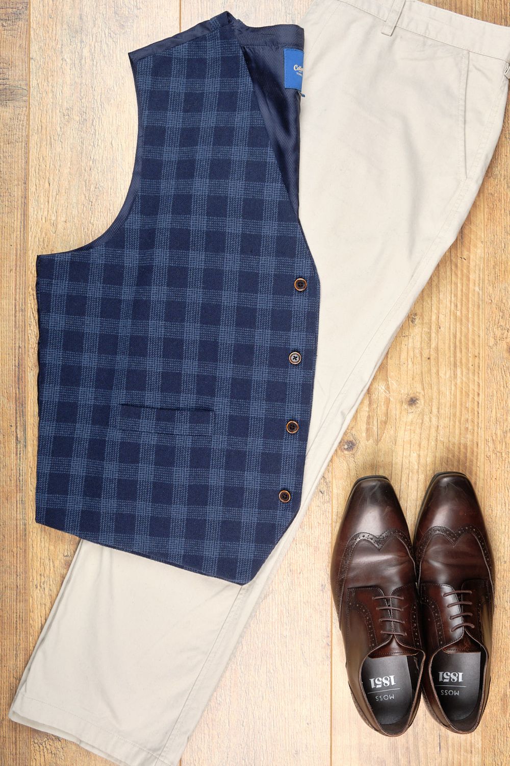 Flatlay of Cotton Traders waistcoat and chinos, and Moss Bros shoes on a light oak background.