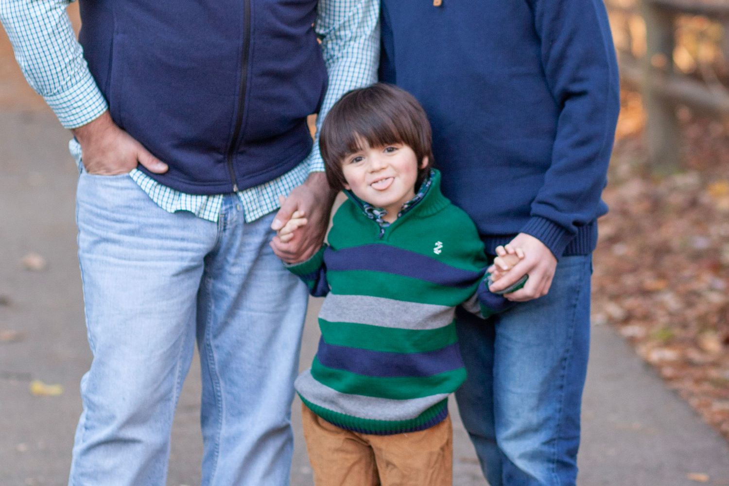 A little dark haired boy holds hands and sticks his tongue out with a smile.