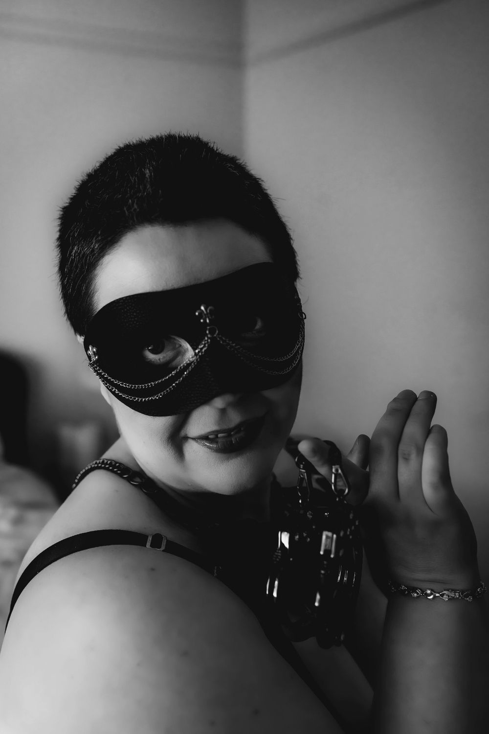 short haired woman in dominatrix mask balancing handcuffs on fingers near face