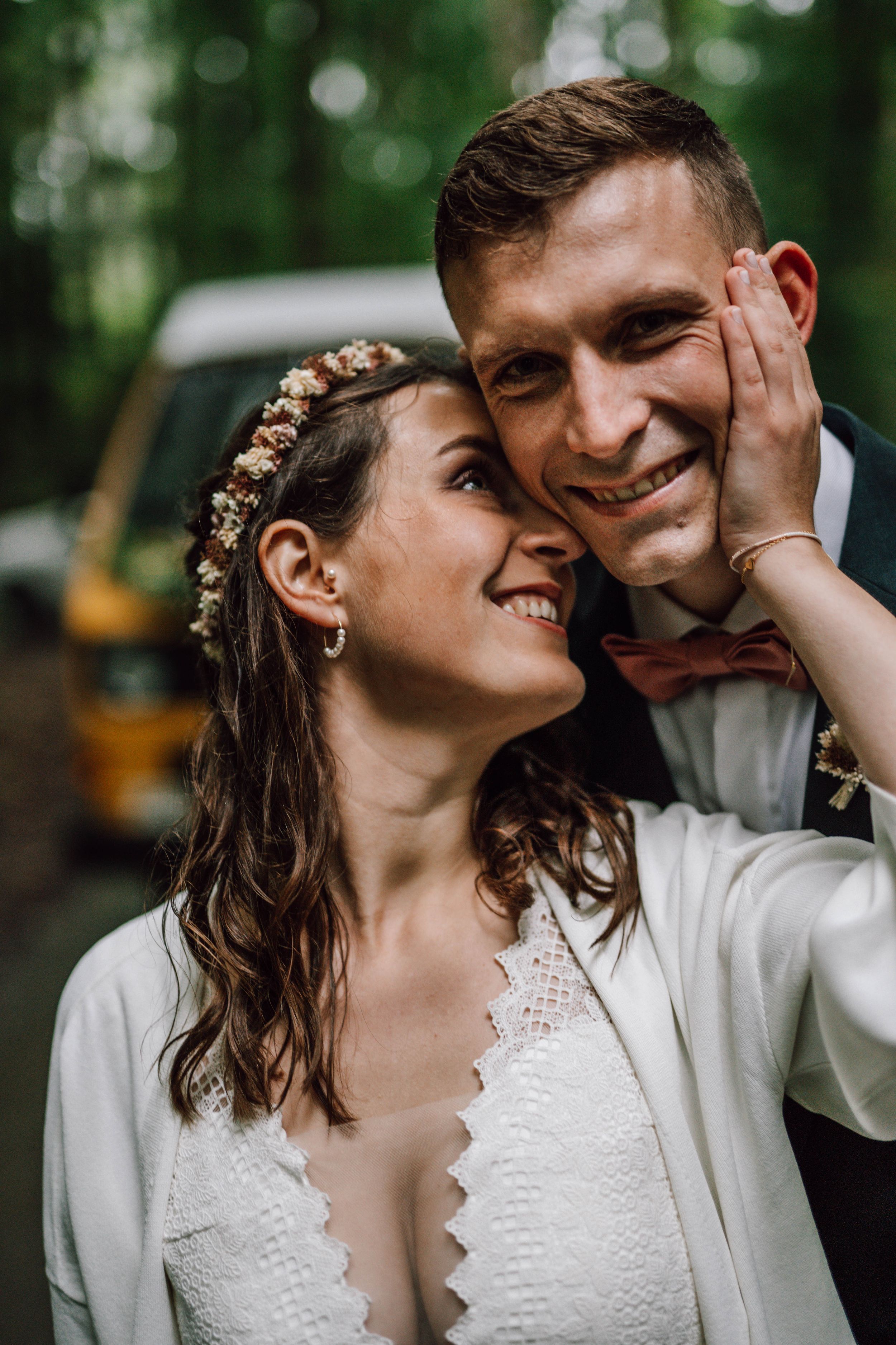 A romantic moment between newlyweds sharing laughter outdoors with natural bokeh background.