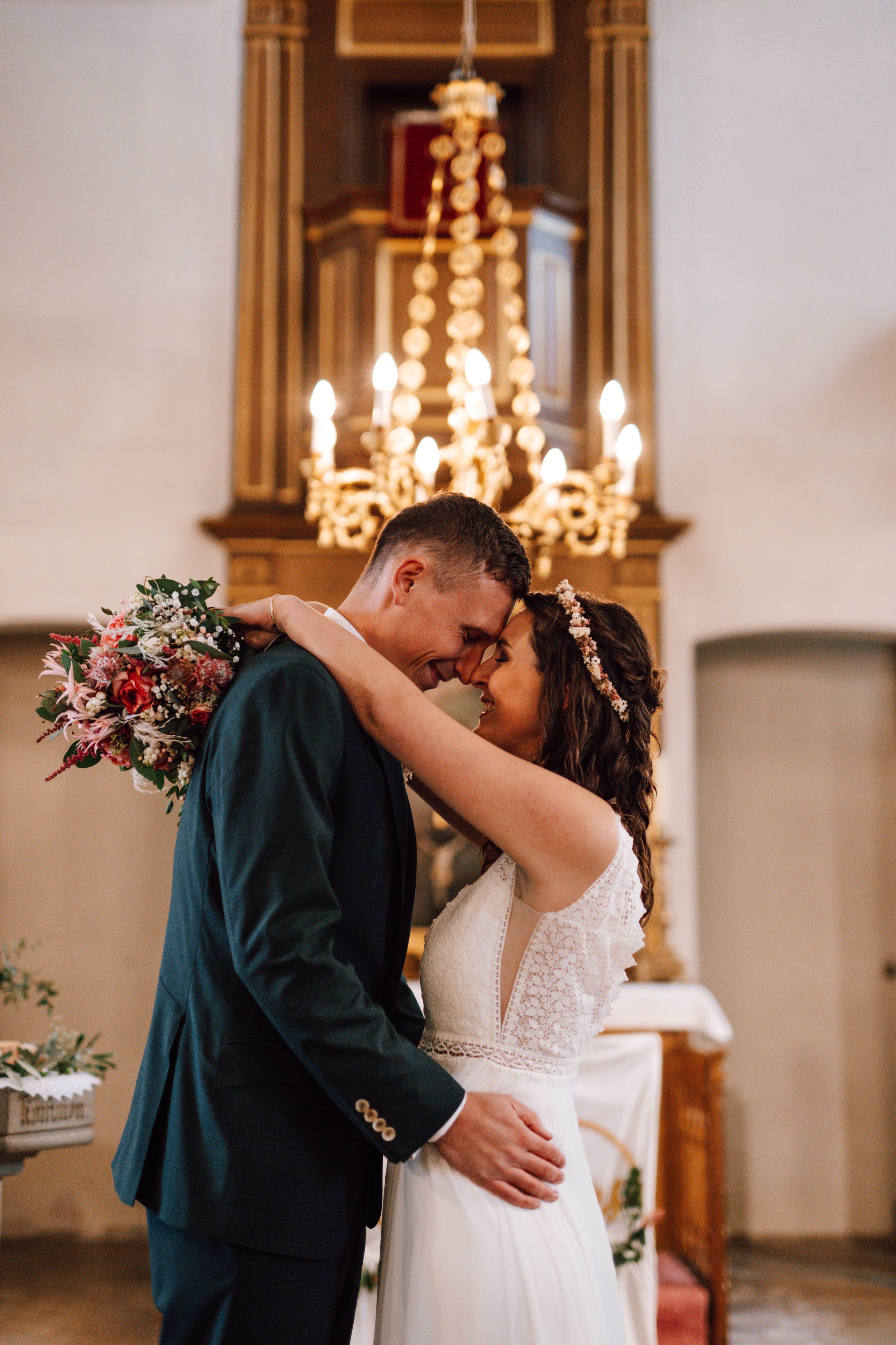Intimate wedding ceremony moment in a church with ornate chandelier and floral decorations.