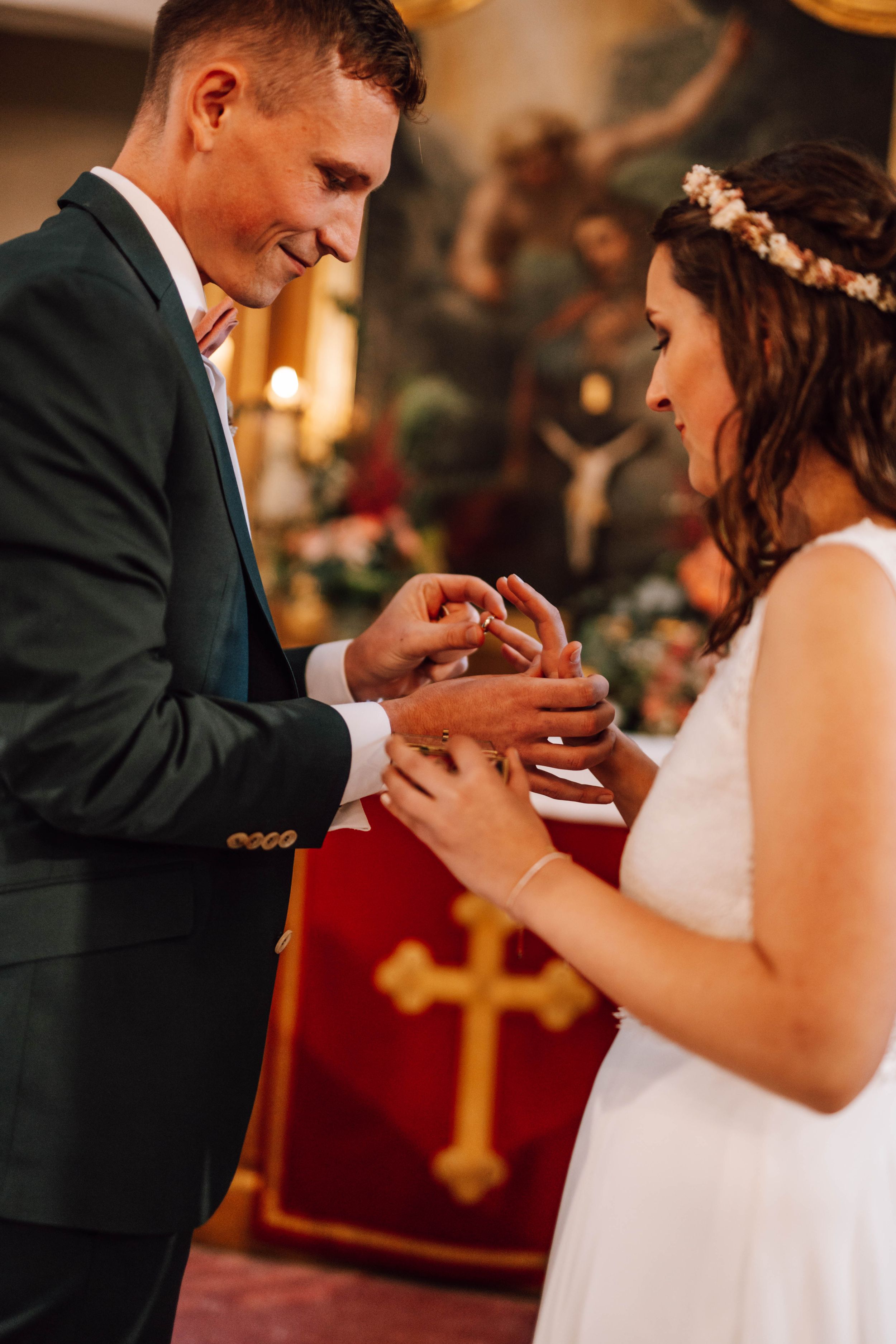Exchange of rings during wedding ceremony with red cross banner in background.