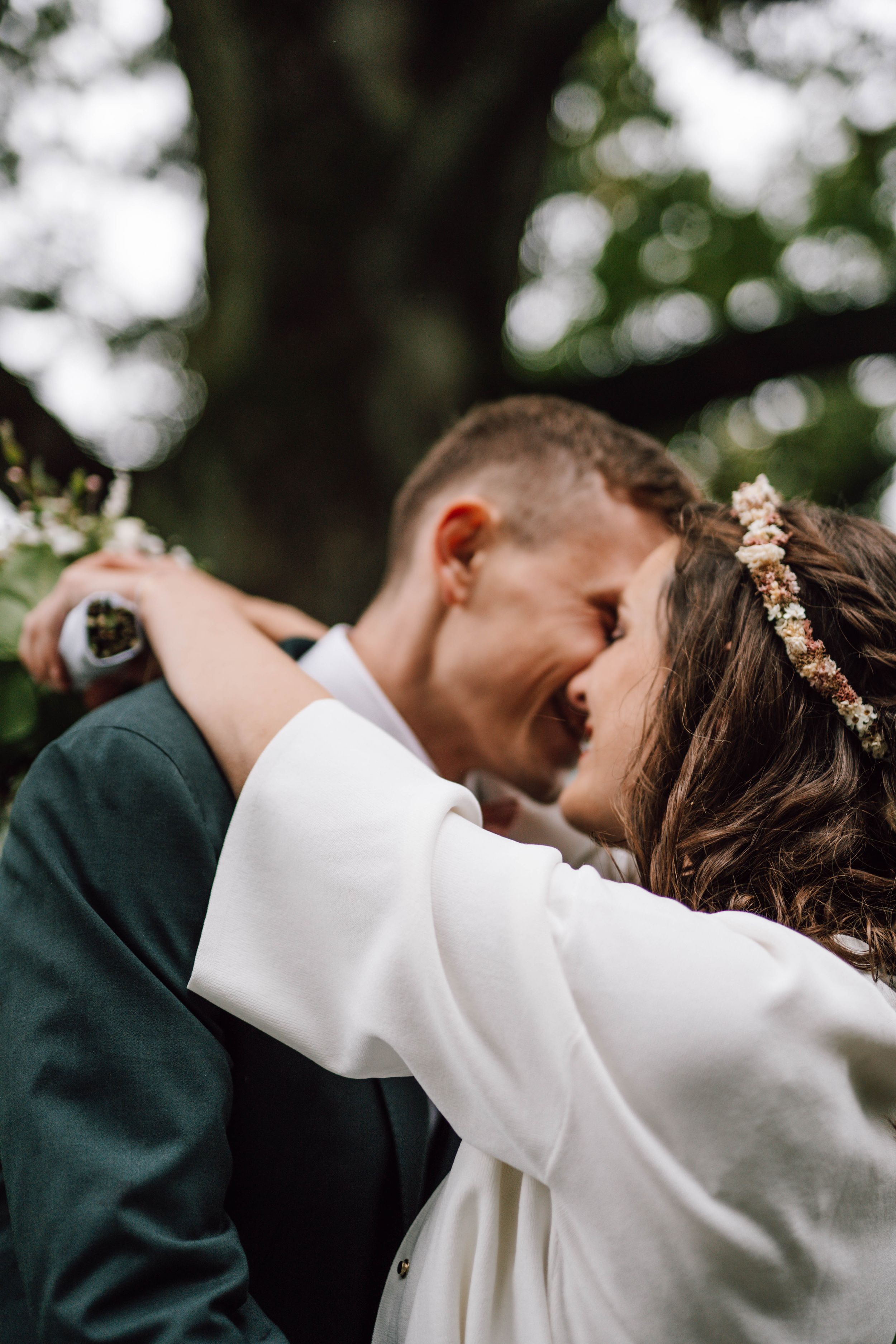 A romantic wedding couple embraces outdoors with bokeh background and the bride wearing a delicate floral crown.