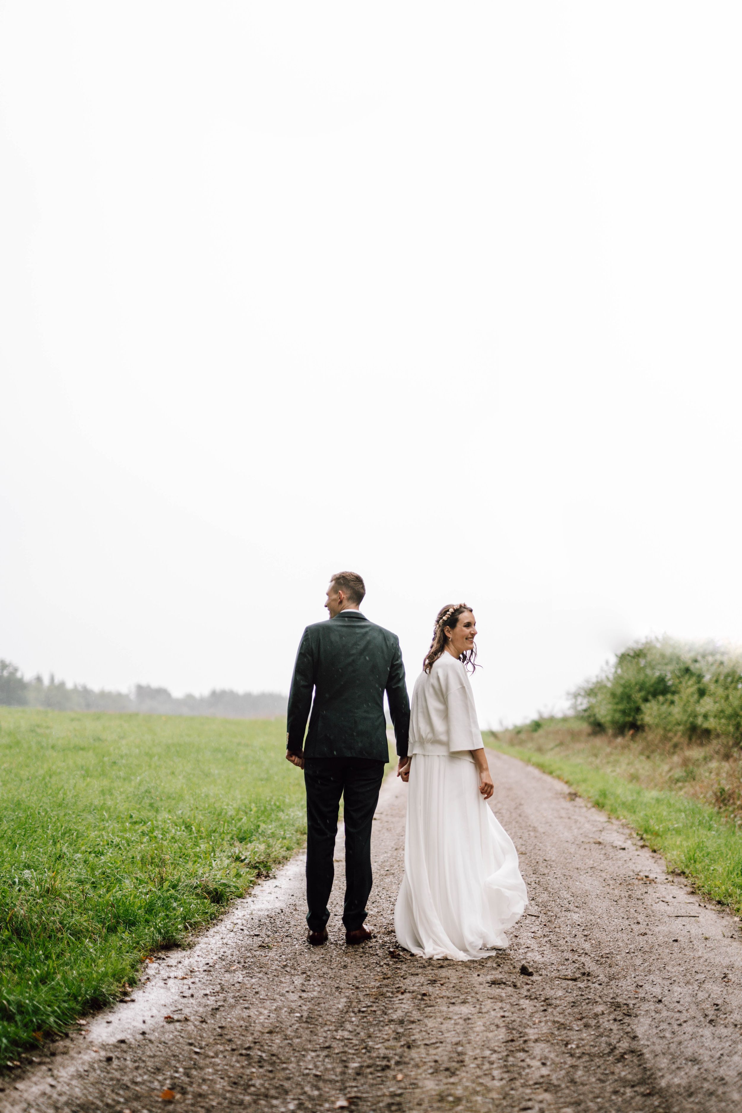 Newlyweds walking down a country path, with bride in white dress and groom in dark green suit.
