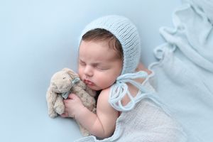 Sleeping newborn wrapped in soft white knit blanket with plush toy companion.