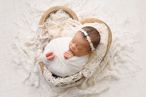 Baby resting in vintage basket surrounded by delicate lace details.