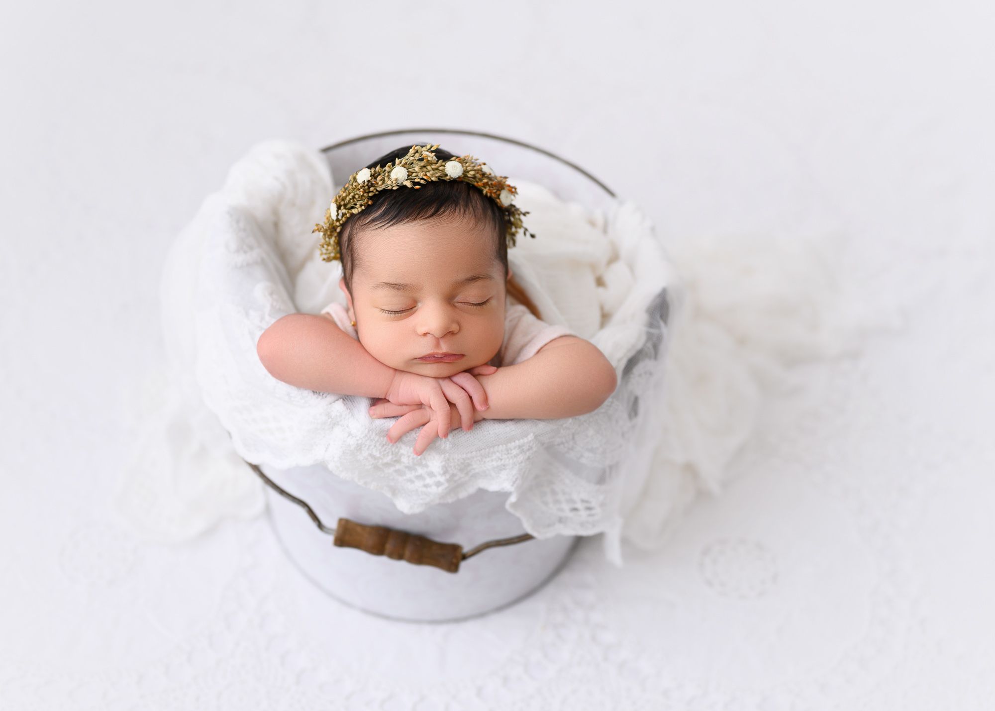 Newborn sleeping peacefully in white lace-trimmed basket.