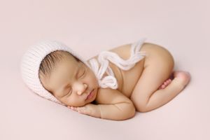 Peaceful newborn baby sleeping on soft pink backdrop wearing delicate bow.