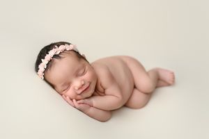 Artistic newborn photography with baby posed on cream backdrop.