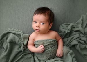 Newborn photography session with baby on sage green textile backdrop.