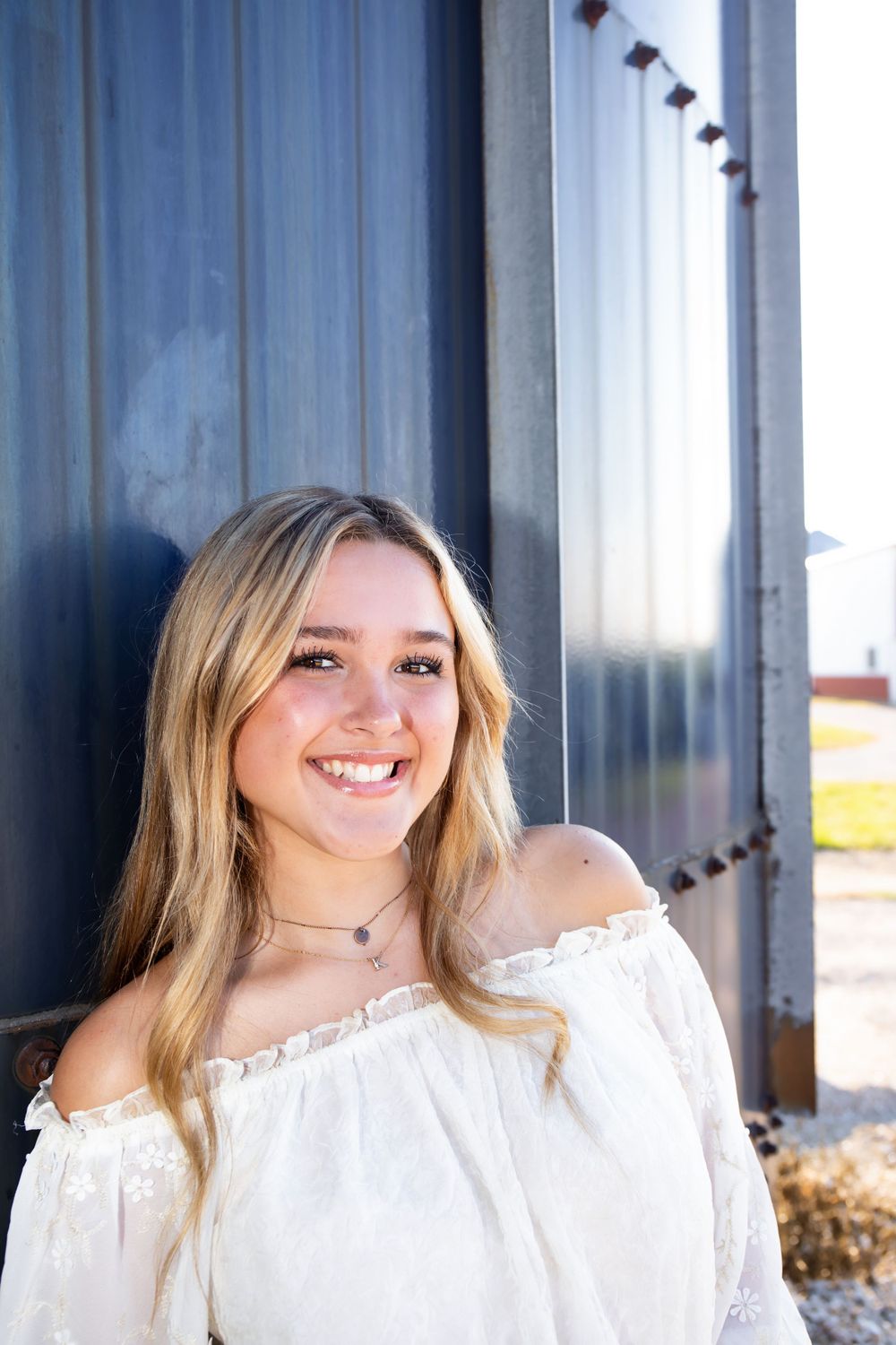 Sunny outdoor portrait against blue metal wall showing casual summer style.
