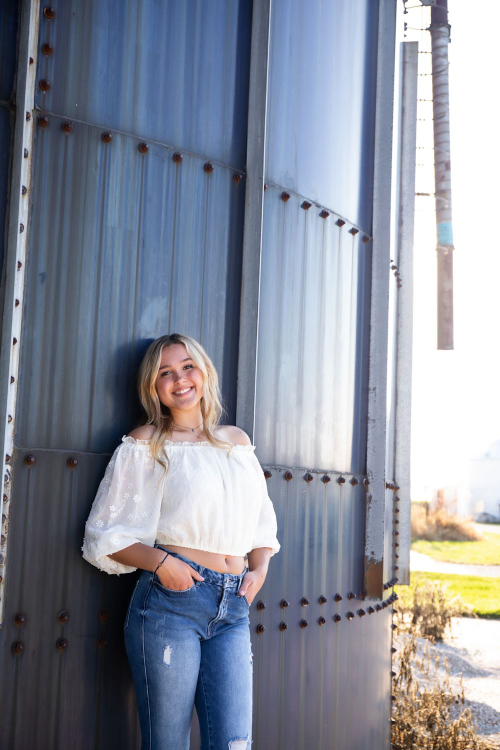 White off-shoulder top and jeans against industrial metal wall background.