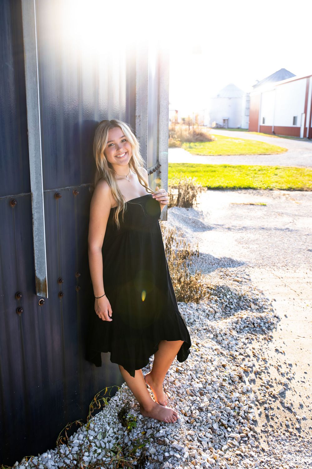 Casual outdoor portrait in black dress with grain silos visible in background.