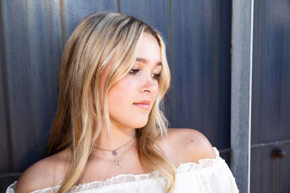 Side profile fashion portrait with delicate necklace and off-shoulder white top.