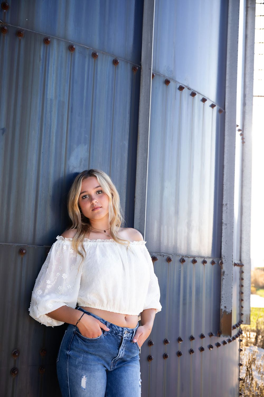 Fashion portrait with blonde hair and casual attire against a metallic corrugated backdrop.