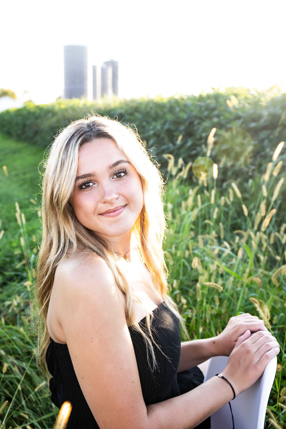 Summer portrait in golden light with tall grain silos and wild grasses in background.