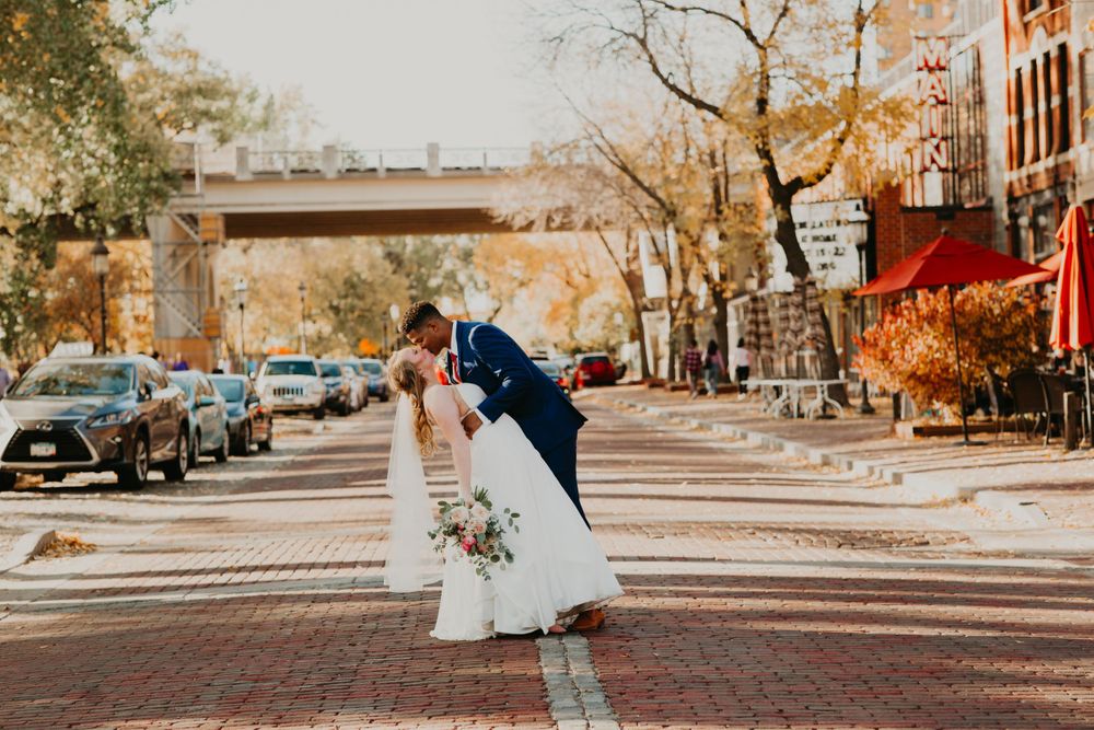Groom dips bride for a kiss in the middle of a charming autumn street lined with colorful trees.