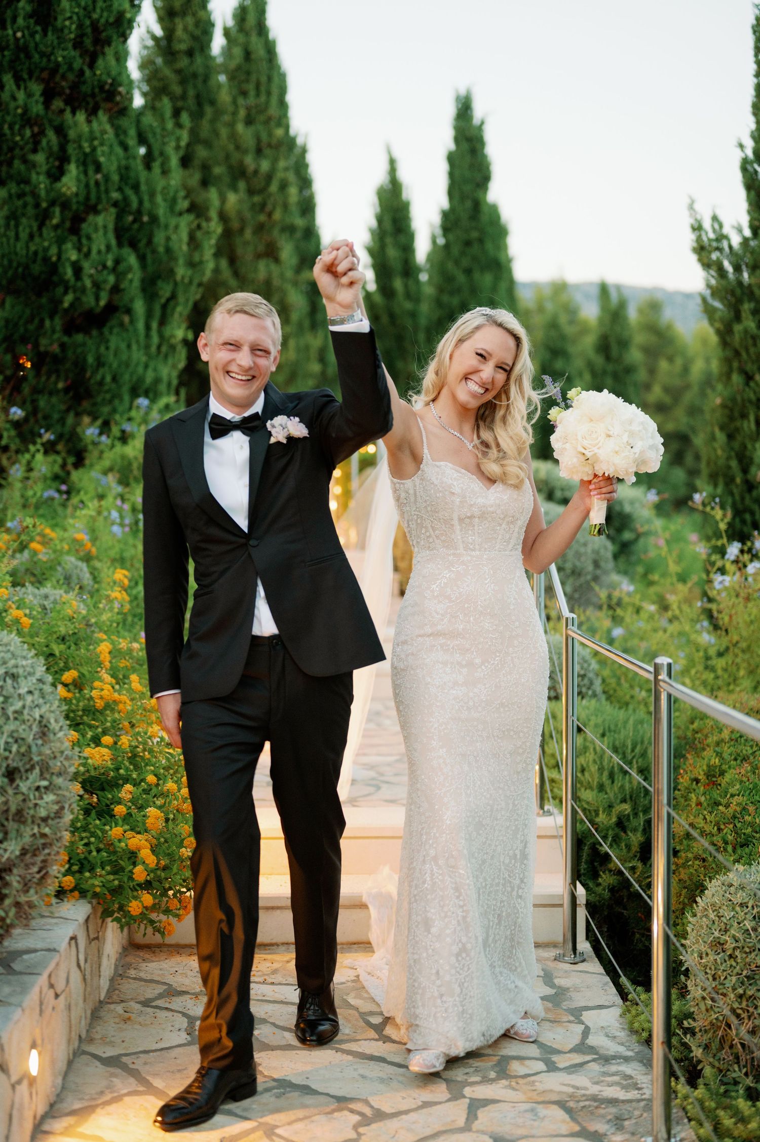 A celebratory moment on garden steps with cypress trees and yellow flowers in the background.