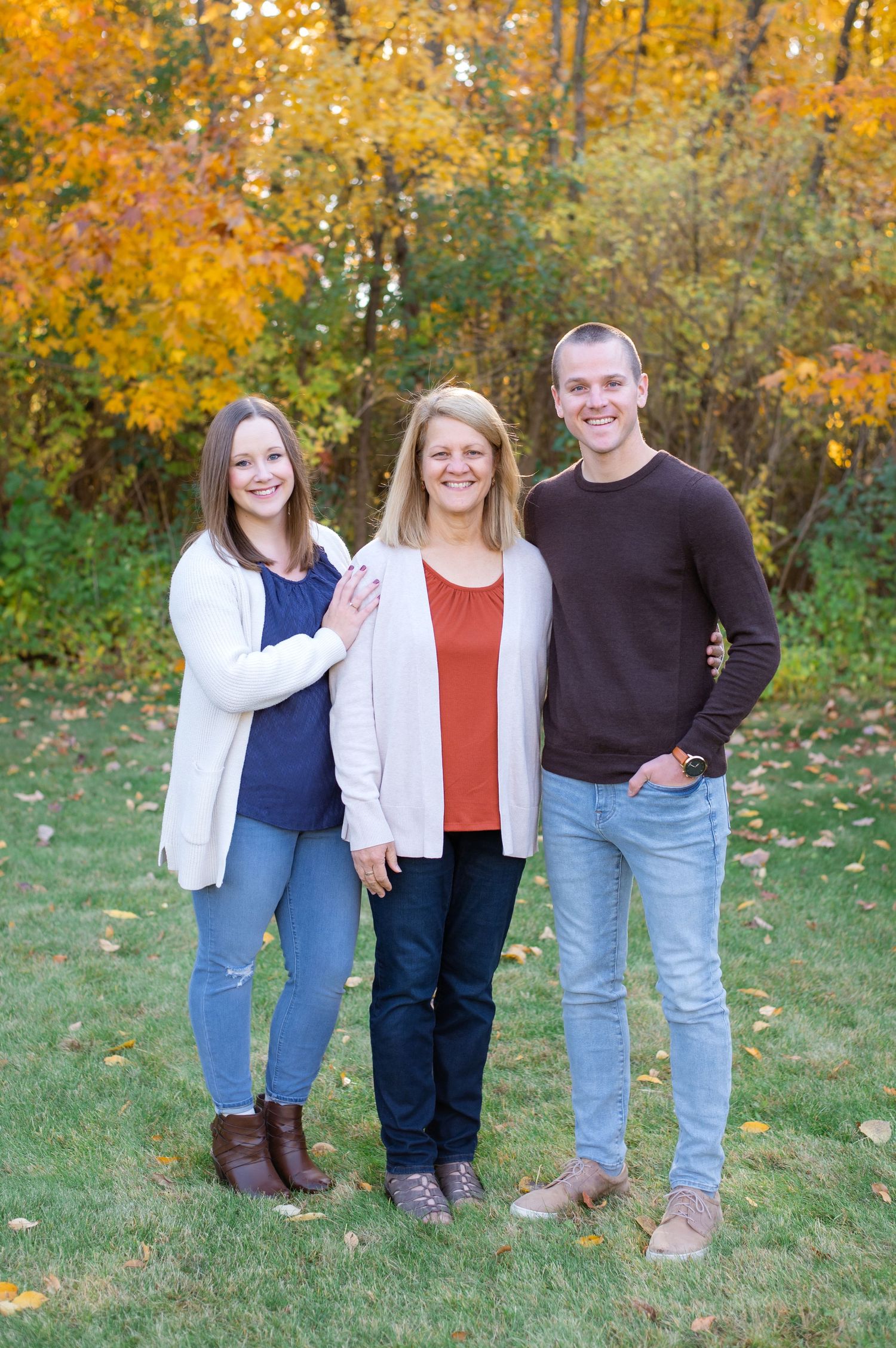 Three people stand together smiling outdoors with vibrant fall colors in the background.