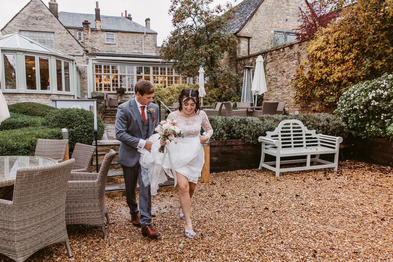 Couple sharing a candid moment during their wedding on a gravel patio with wicker furniture and autumn foliage.