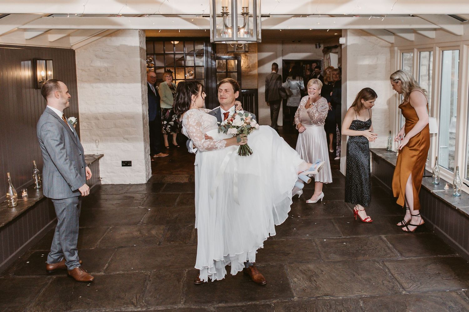 Wedding guests watching as newlyweds make grand entrance being carried into reception hall.