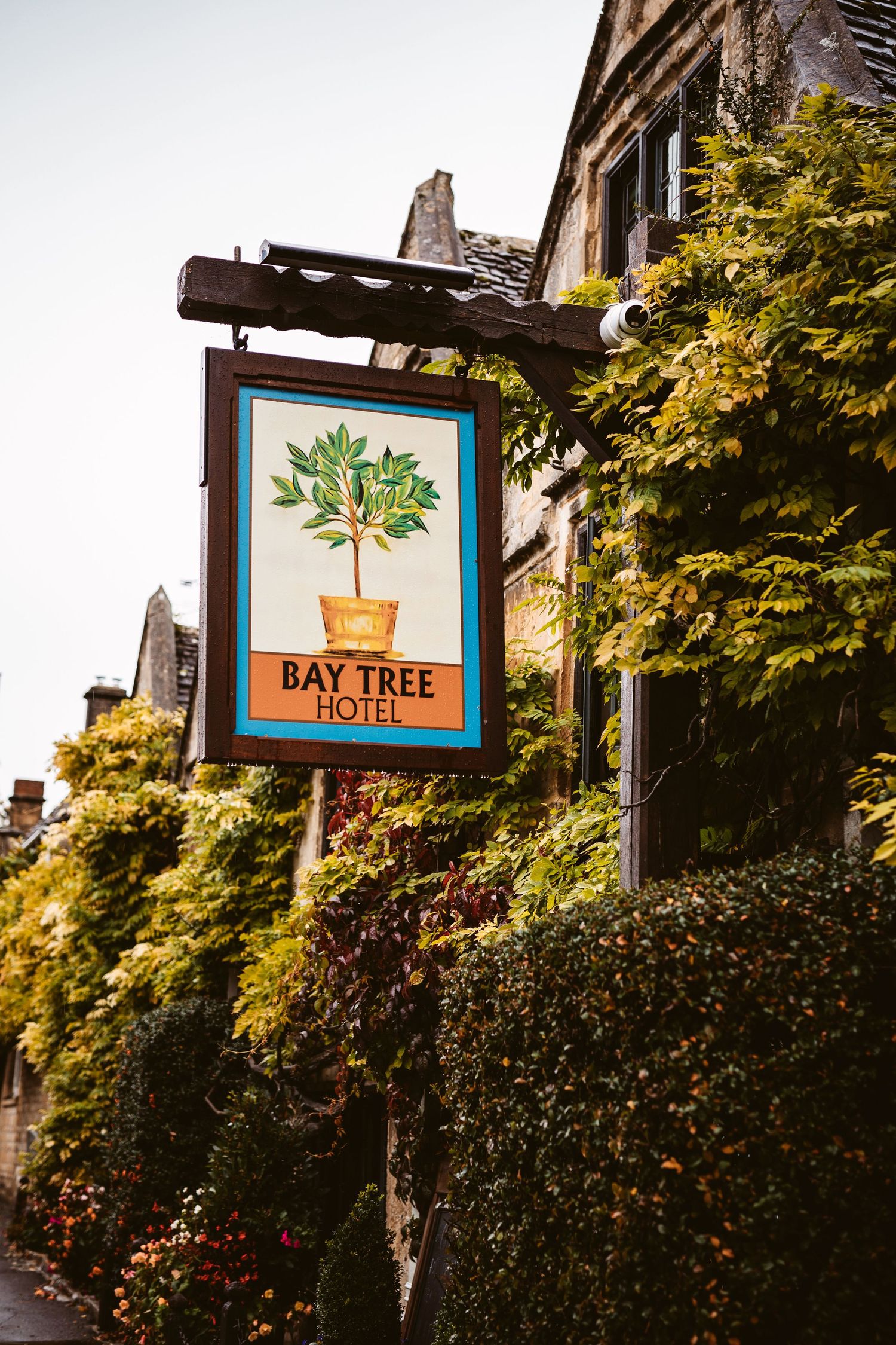 A rustic pub sign for the Bay Tree Hotel mounted on an ivy-covered stone wall.