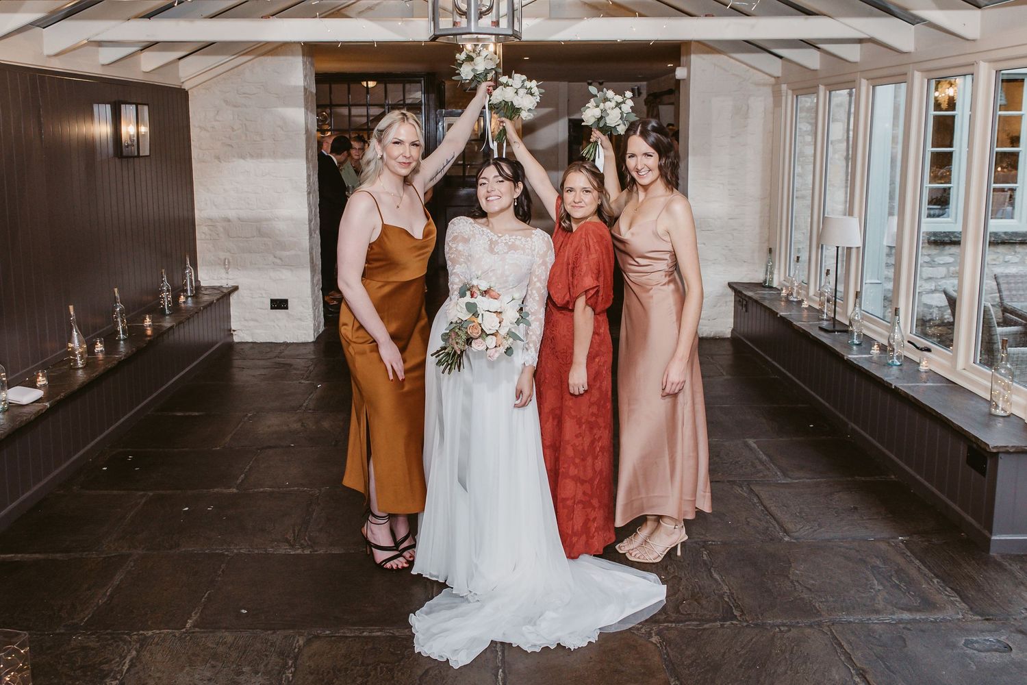 Bridal party wearing autumn-colored dresses pose together in an elegant indoor setting.