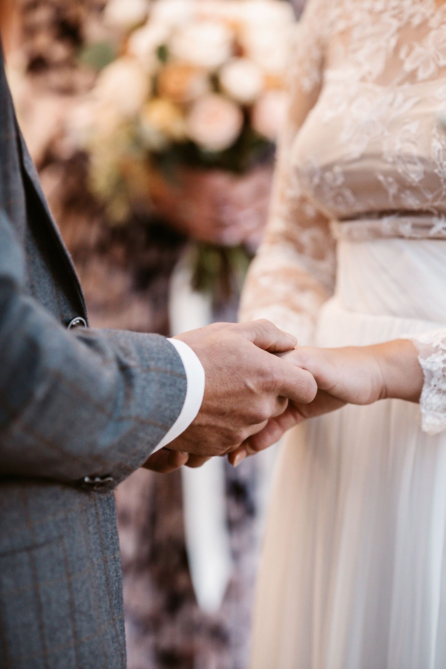 Close up of hands exchanging rings during wedding ceremony with lace dress detail.