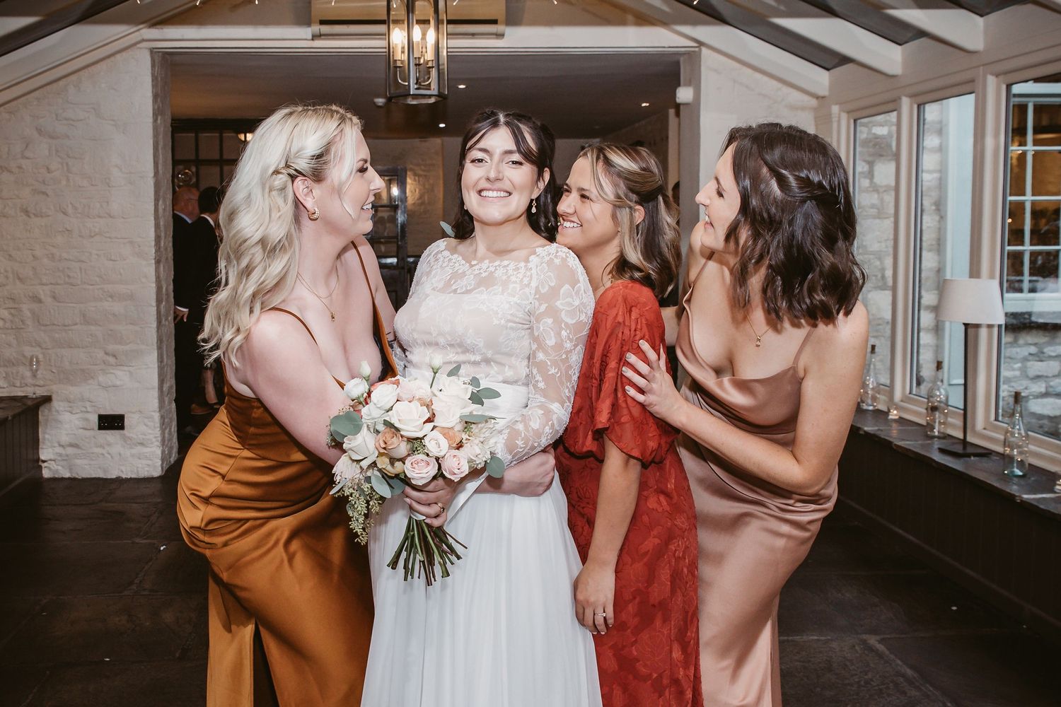 Bridal party in silk dresses shares candid laughing moment during wedding photos.