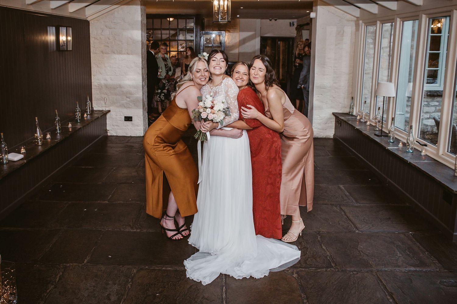 Wedding party in rust, white and burgundy dresses share intimate moment in elegant venue.