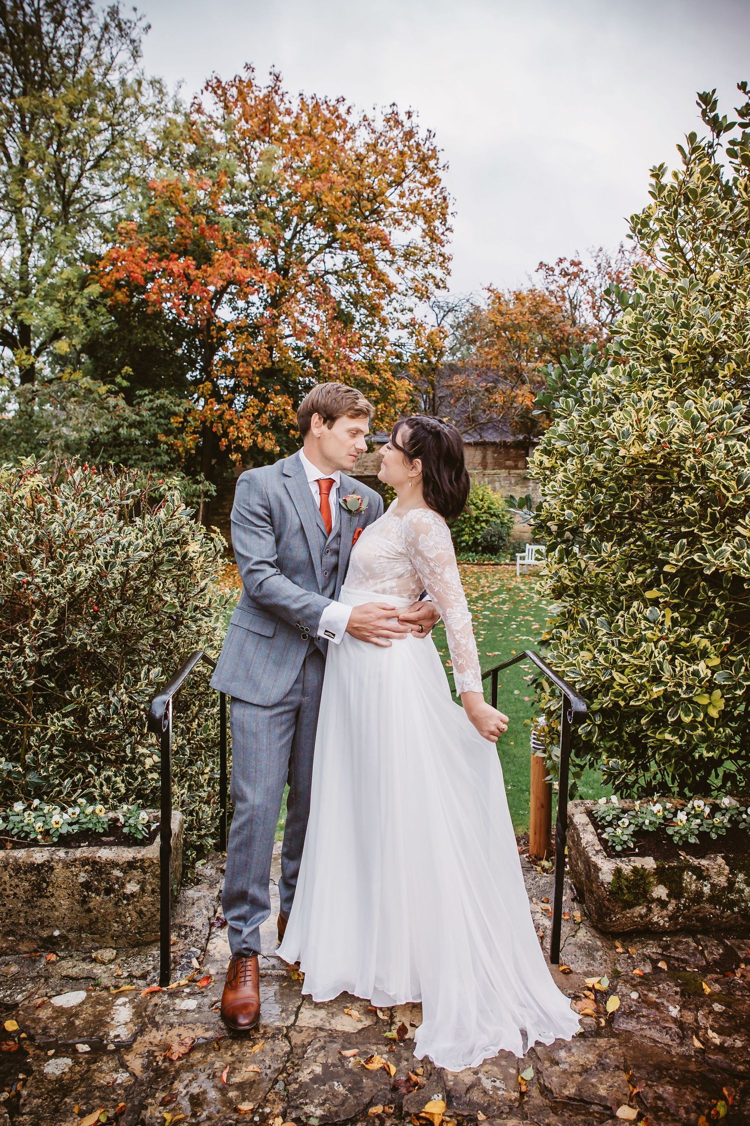 Romantic autumn wedding photo with couple on stone steps surrounded by colorful foliage.